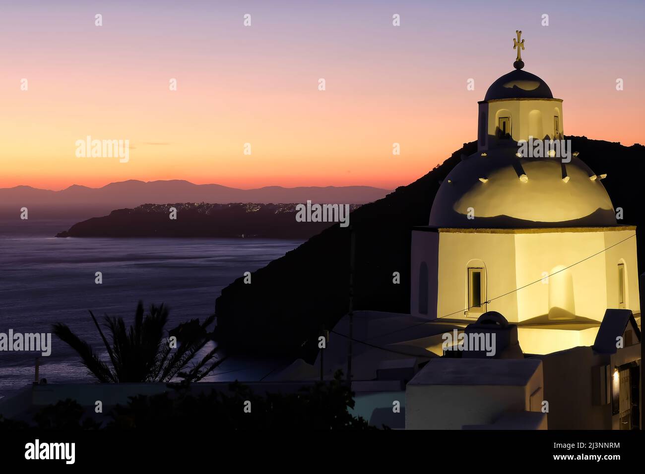 Vista di una bella chiesa ortodossa bianca e Oia Santorini sullo sfondo, mentre il sole tramonta in modo drammatico Foto Stock