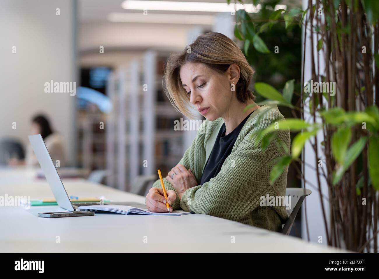 Carriera accademica. Professore universitario femminile che prende appunti in giorno pianificatore mentre si siede in biblioteca Foto Stock