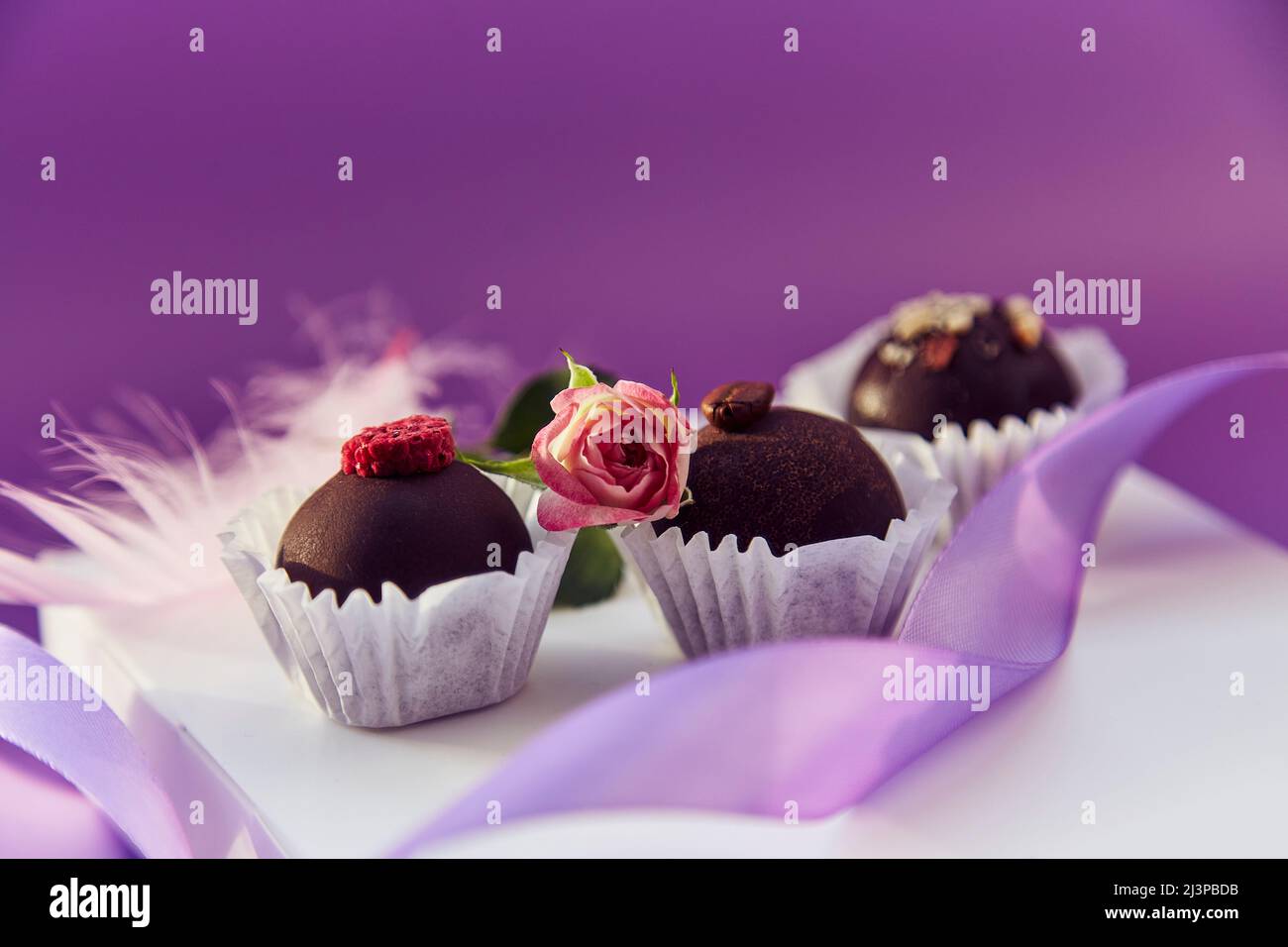Dolci al cioccolato natalizi. Delicate piume rosa e nastro viola. Motivo di colore viola con spazio di copia Foto Stock
