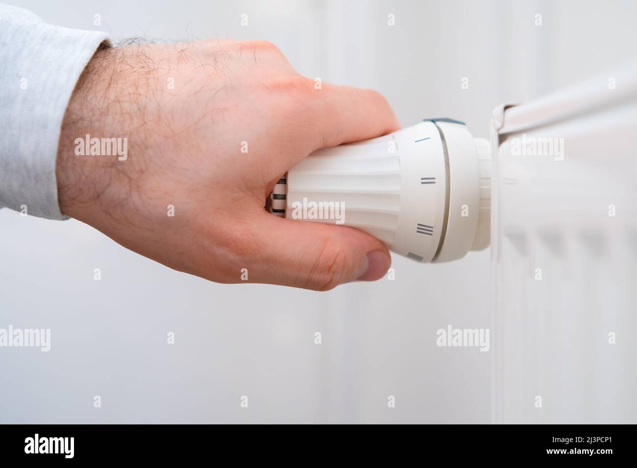 Man Hand regola la manopola di regolazione della temperatura del radiatore di riscaldamento per ridurre i costi di riscaldamento. Foto Stock