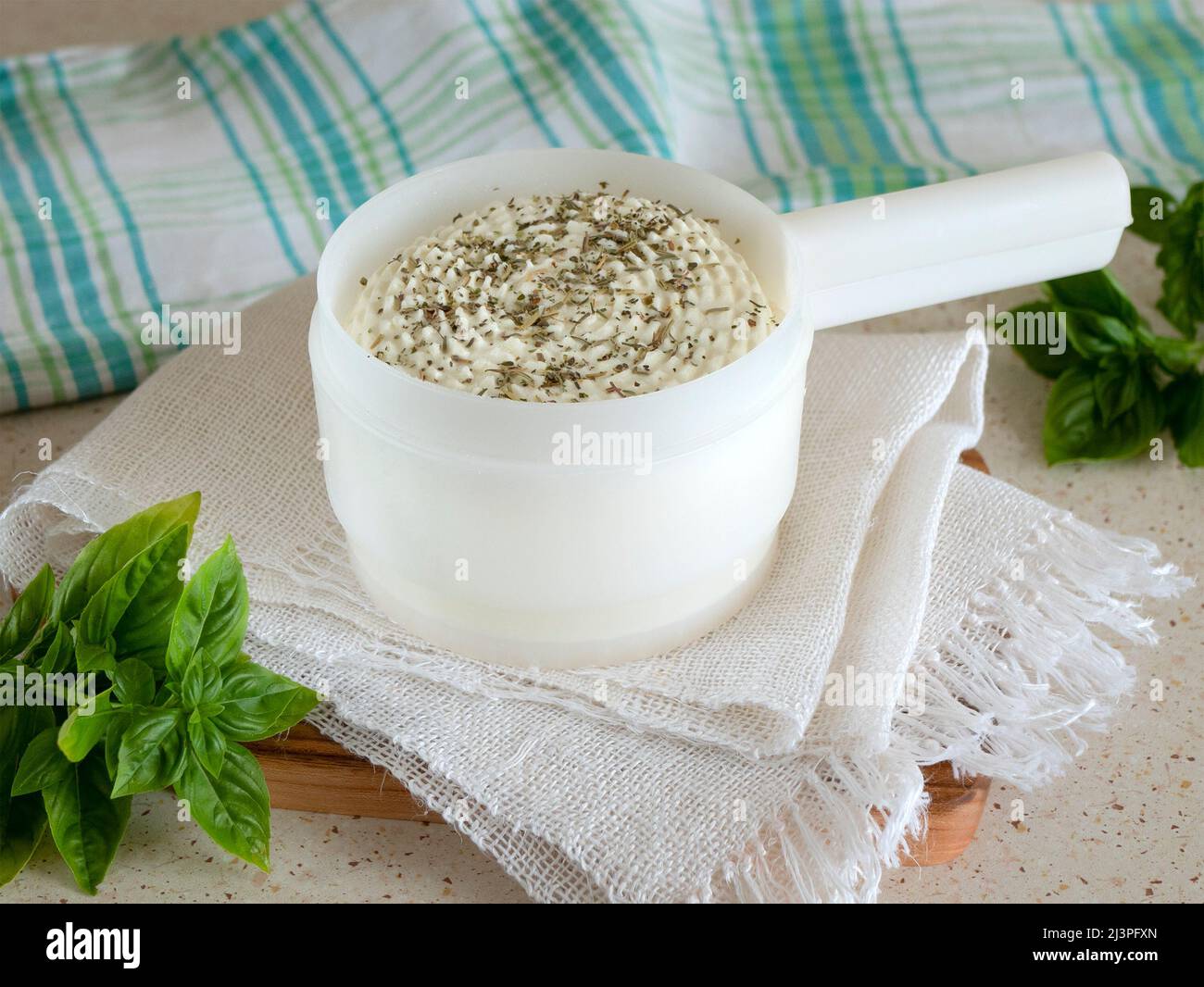 Arrotonda il formaggio casolare in uno stampo per la produzione di formaggio con erbe secche e basilico fresco, fuoco selettivo. Latticini fatti in casa Foto Stock