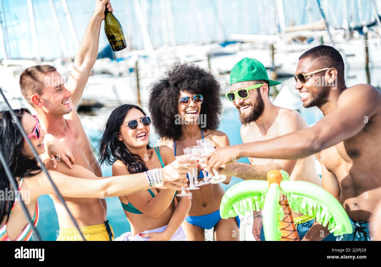 Amici alla moda che si divertono a tostare vino champagne al party in barca a vela - amicizia e concetto di stile di vita di viaggio con persone multiculturali Foto Stock