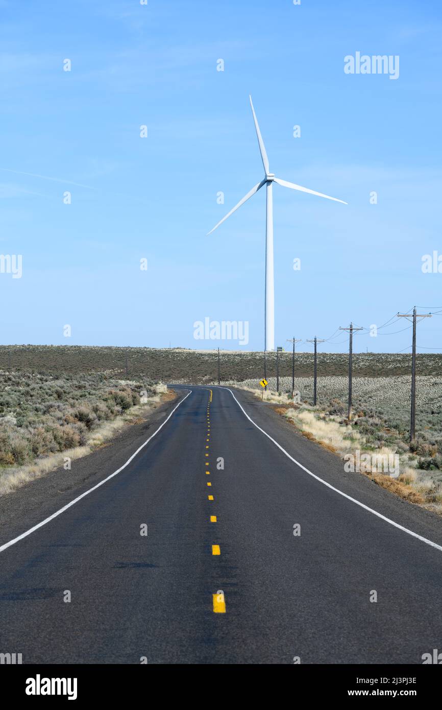 Strada nello stato centrale di Washington in lontananza con una turbina eolica con una linea punteggiata gialla e cielo blu Foto Stock
