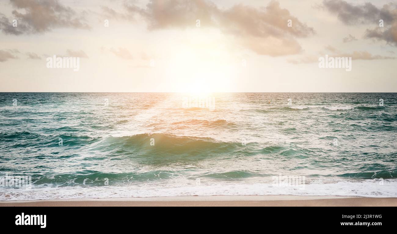 I soli si stanno abbassando, lasciando fluire le onde. Scatto di un bellissimo tramonto sull'oceano. Foto Stock
