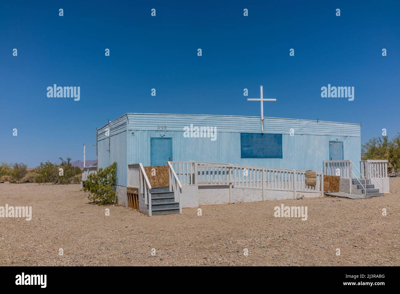 Una chiesa di rimorchio blu a Slab City, California, con una croce di legno bianca sulla parte superiore e con scale su entrambe le estremità. La chiesa è accessibile da ADA attraverso un lungo Foto Stock