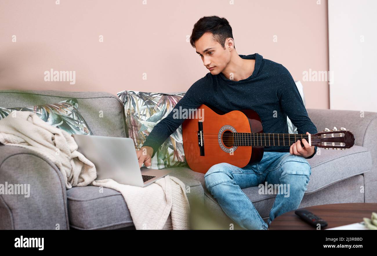Quali lezioni vi hanno insegnato il blocco. Scatto di un giovane che usa un computer portatile mentre suona la chitarra a casa. Foto Stock