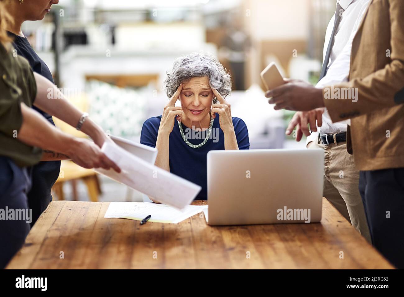 Teso da tante difficoltà. Ripresa ritagliata di una donna d'affari stressata circondata da colleghi che hanno bisogno di aiuto in un ufficio. Foto Stock