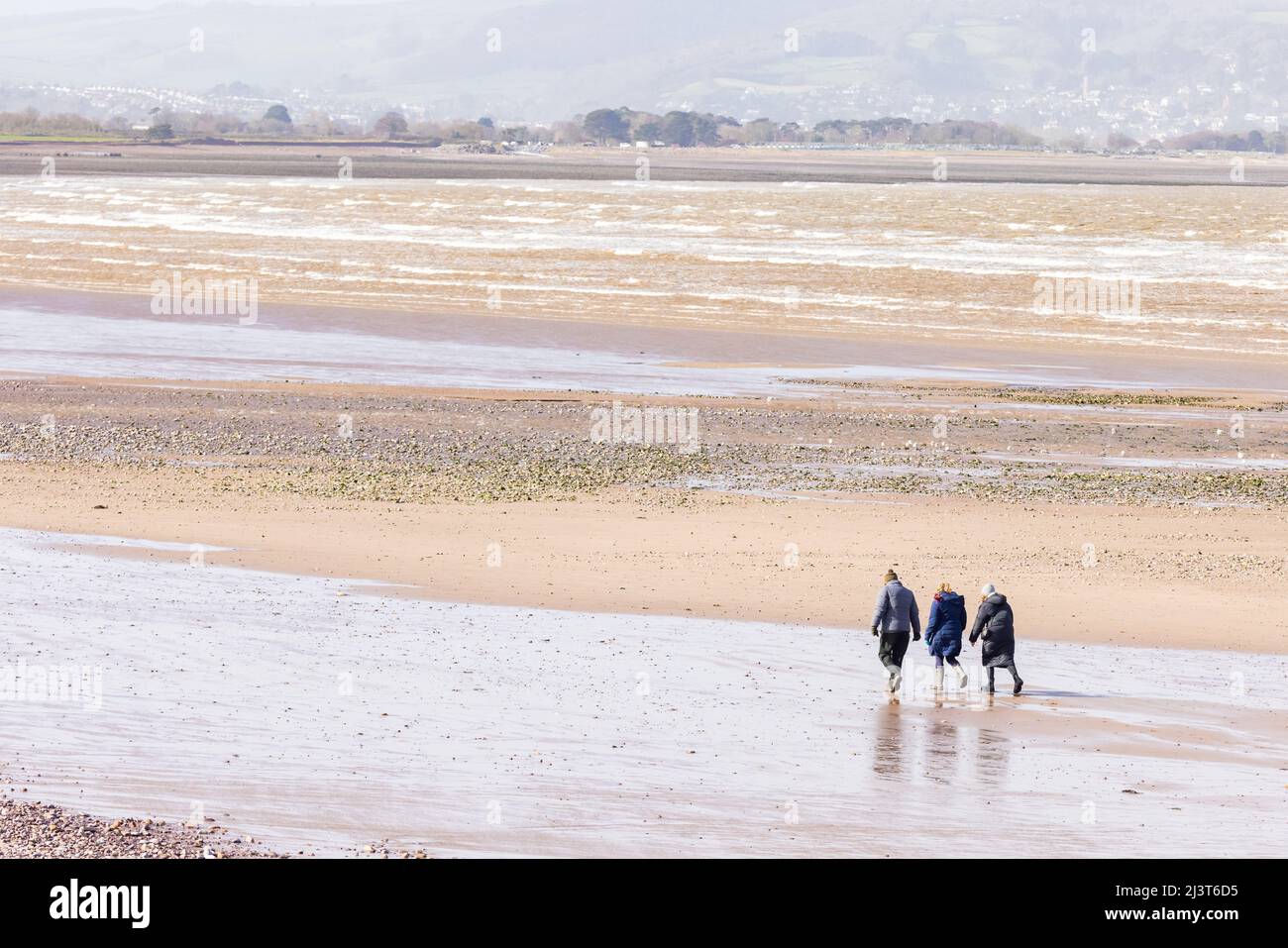 Tre persone camminano di fronte alla spiaggia a bassa marea, Blue Anchor, Somerset, Regno Unito Foto Stock
