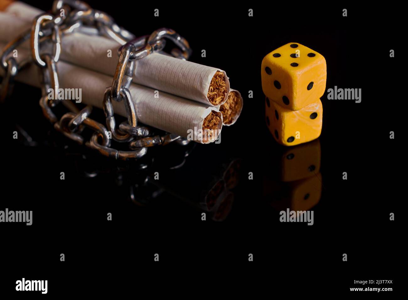 Nicotina e dipendenza da gioco d'azzardo. Sigarette, riavvolte da una catena e da due dadi Foto Stock