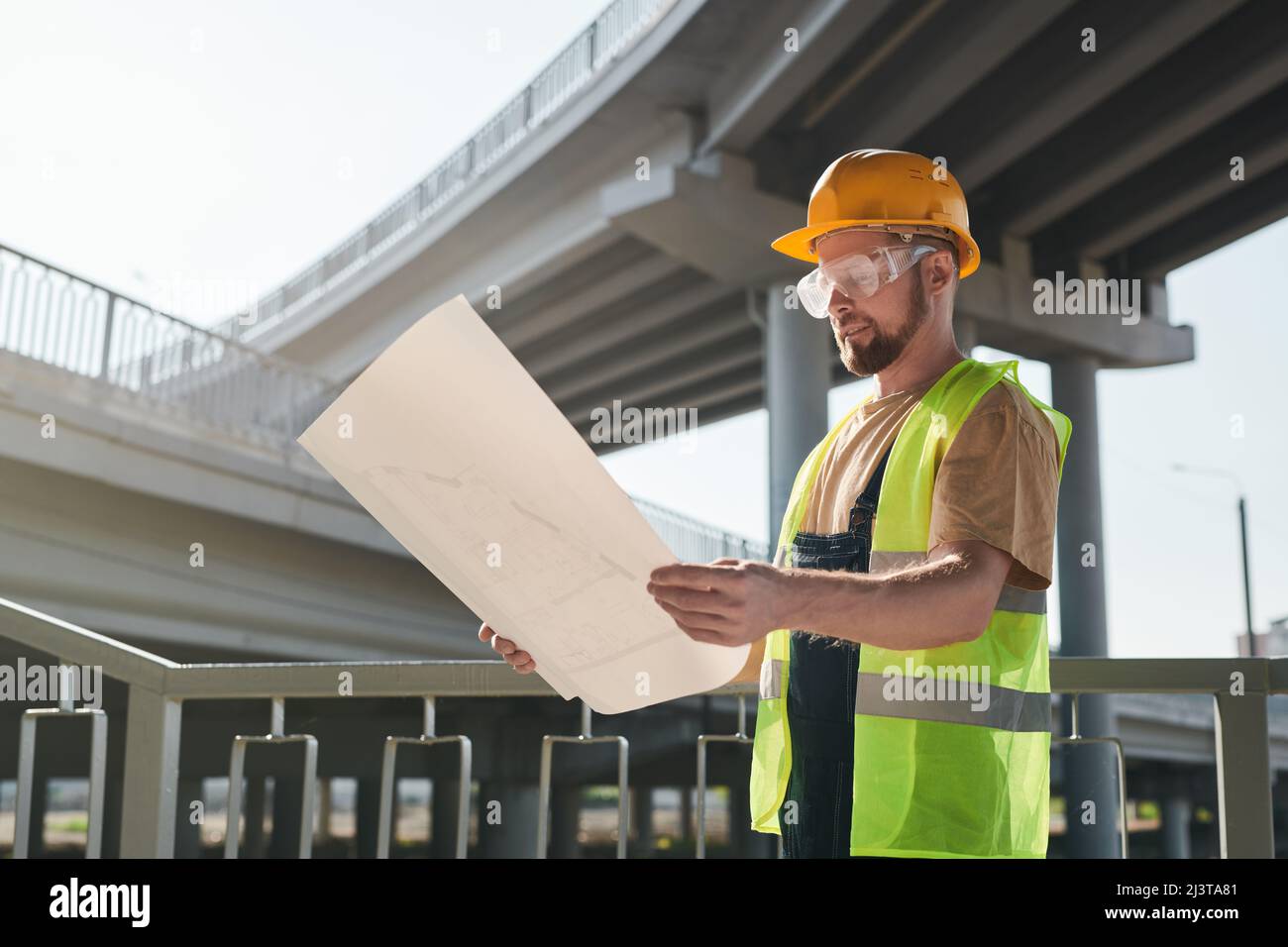 Lavoratore di costruzione che esamina il progetto e in piedi sul sito di costruzione di casa d'appartamento, grande blocco di appartamenti in costruzione Foto Stock