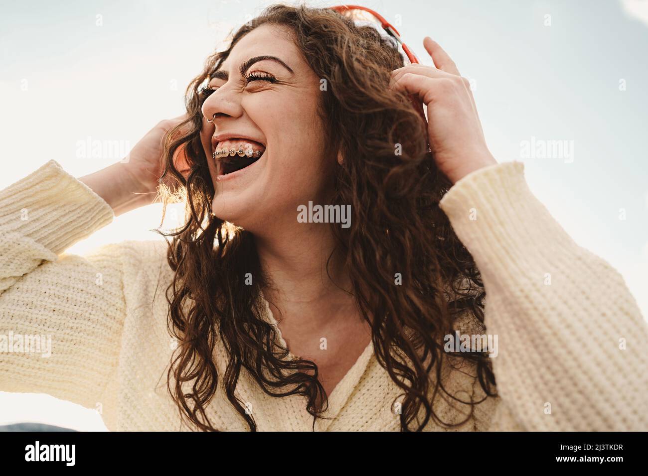 Ragazza felice con un ampio sorriso mostrando un dente di brace - Gen z donna che indossa cuffie wireless rosso all'aperto Foto Stock