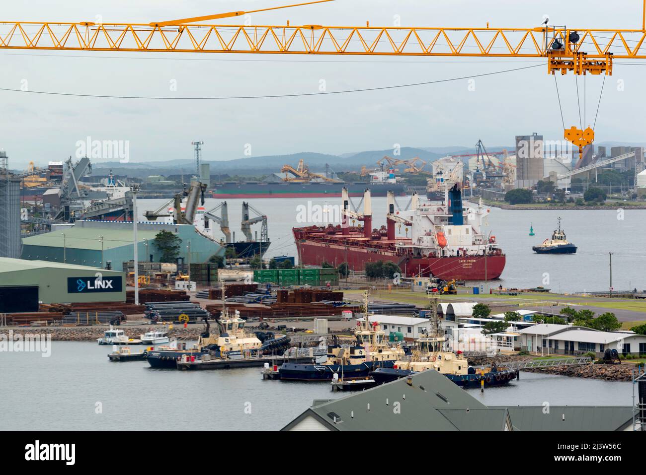 Un braccio di gru sembra galleggiare su navi e rimorchiatori ormeggiati nella zona industriale di Carrington del Porto di Newcastle, nuovo Galles del Sud, Australia Foto Stock