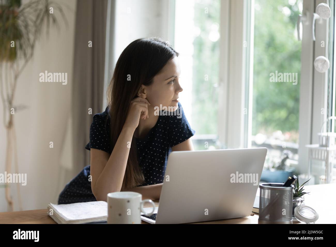 Donna premurosa seduta al tavolo con laptop guarda fuori finestra Foto Stock