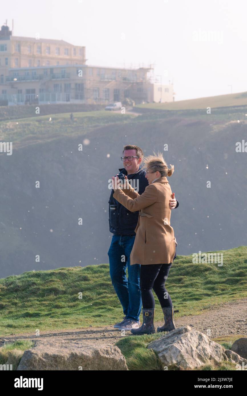 Una donna che fotografa il clima selvaggio mentre la schiuma di mare soffiata in aria dal vento della forza della tempesta mentre Storm Eunice raggiunge Newquay in Cornovaglia. Foto Stock