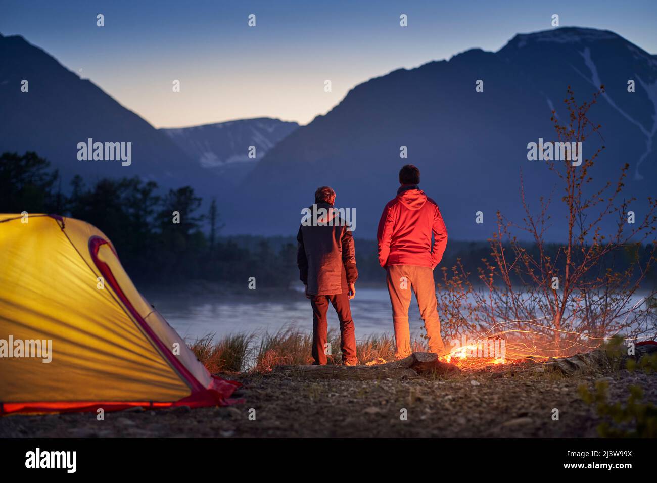 Due turisti in piedi in tenda con falò e guardando la montagna. Campeggio nella zona selvaggia Foto Stock