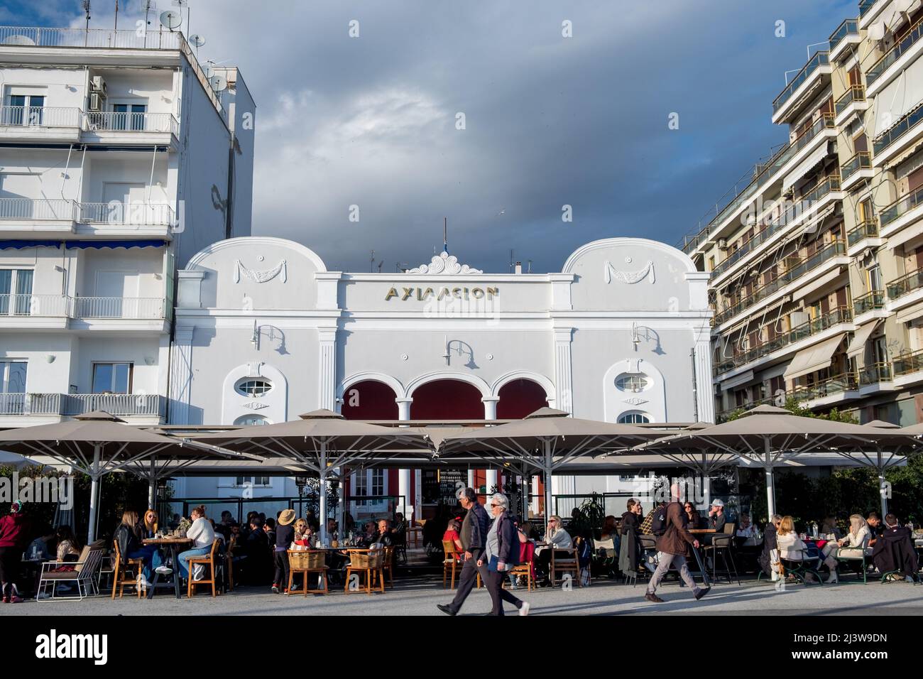 Le persone che camminano sul marciapiede e gli altri che si siedono e si godono il loro caffè nella città di Volos, Grecia Foto Stock