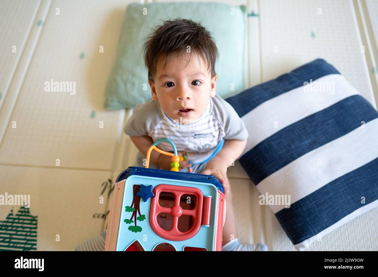 bambino di 8 mesi di razza mista che gioca con box attività in camera da letto mentre si siede sul pavimento coperto da un tappetino gioco di gomma Foto Stock