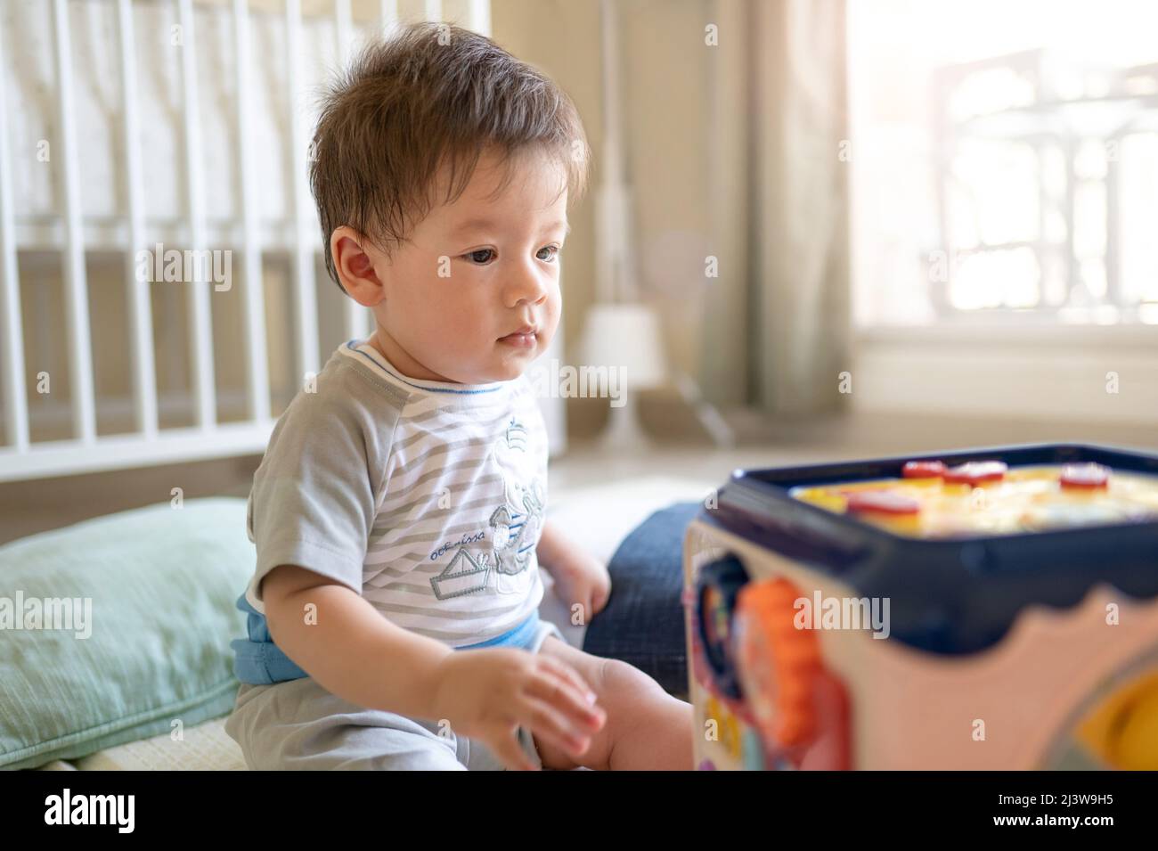 bambino di 8 mesi di razza mista che gioca con box attività in camera da letto mentre si siede sul pavimento coperto da un tappetino gioco di gomma Foto Stock