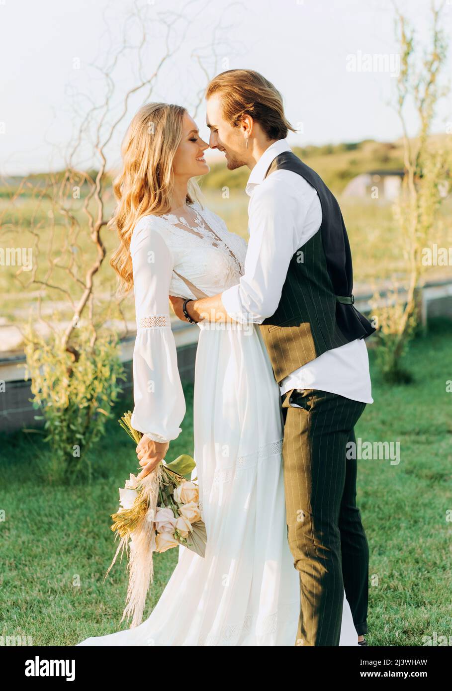 Coppia elegante di sposi allegri che camminano sul campo il loro giorno di nozze con bouquet Foto Stock