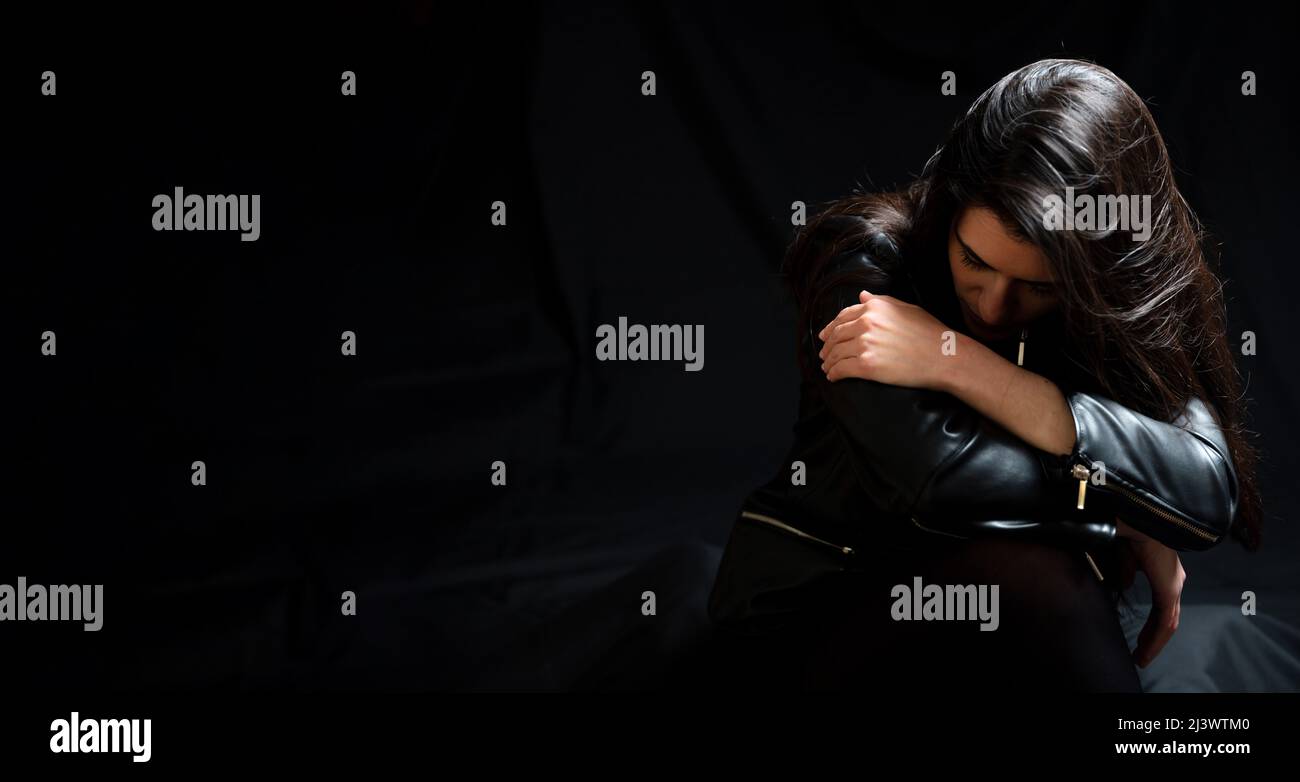 Giovane donna in giacca nera in pelle, triste e solitario profondo nei pensieri in una stanza buia. Depressione e concetto di dolore Foto Stock
