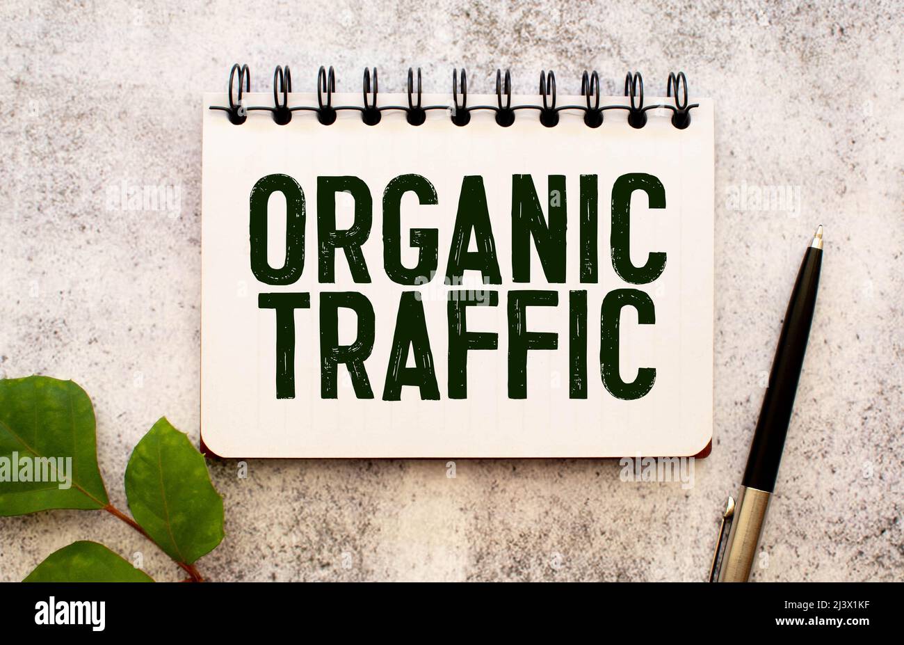 Traffico biologico - business concept testo su un taccuino bianco e orologio a clessidra, foglie verdi di fiori. Foto Stock