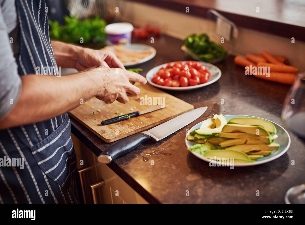 Ogni pasto è un lavoro d'amore. Scatto ritagliato di un giovane uomo inidentificabile che trita verdure nella sua cucina a casa. Foto Stock