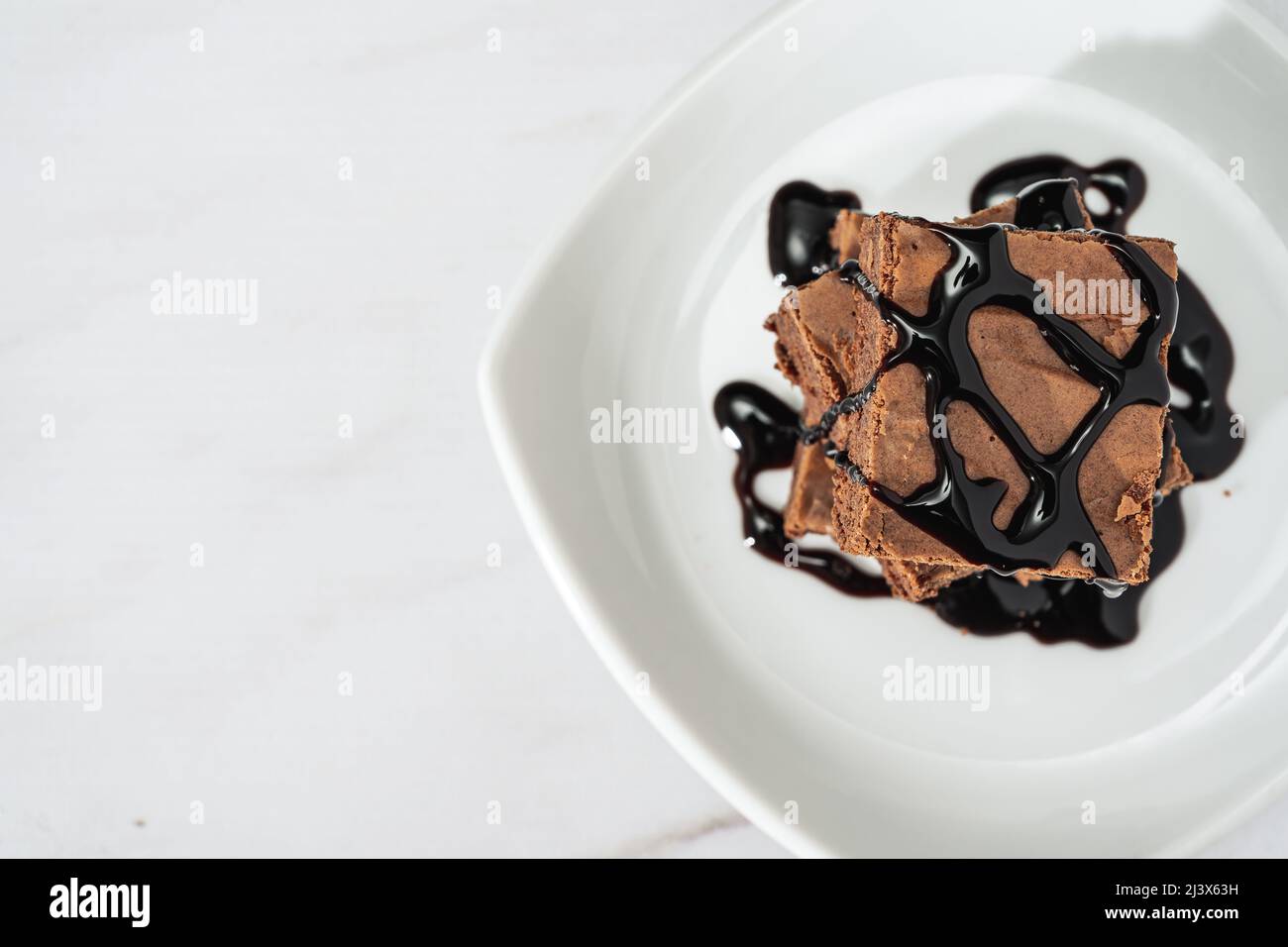 mucchio di brownie di cioccolato con ciocche di salsa di cioccolato su un piatto bianco su un tavolo di marmo. Vista dall'alto. Spazio di copia. Foto Stock