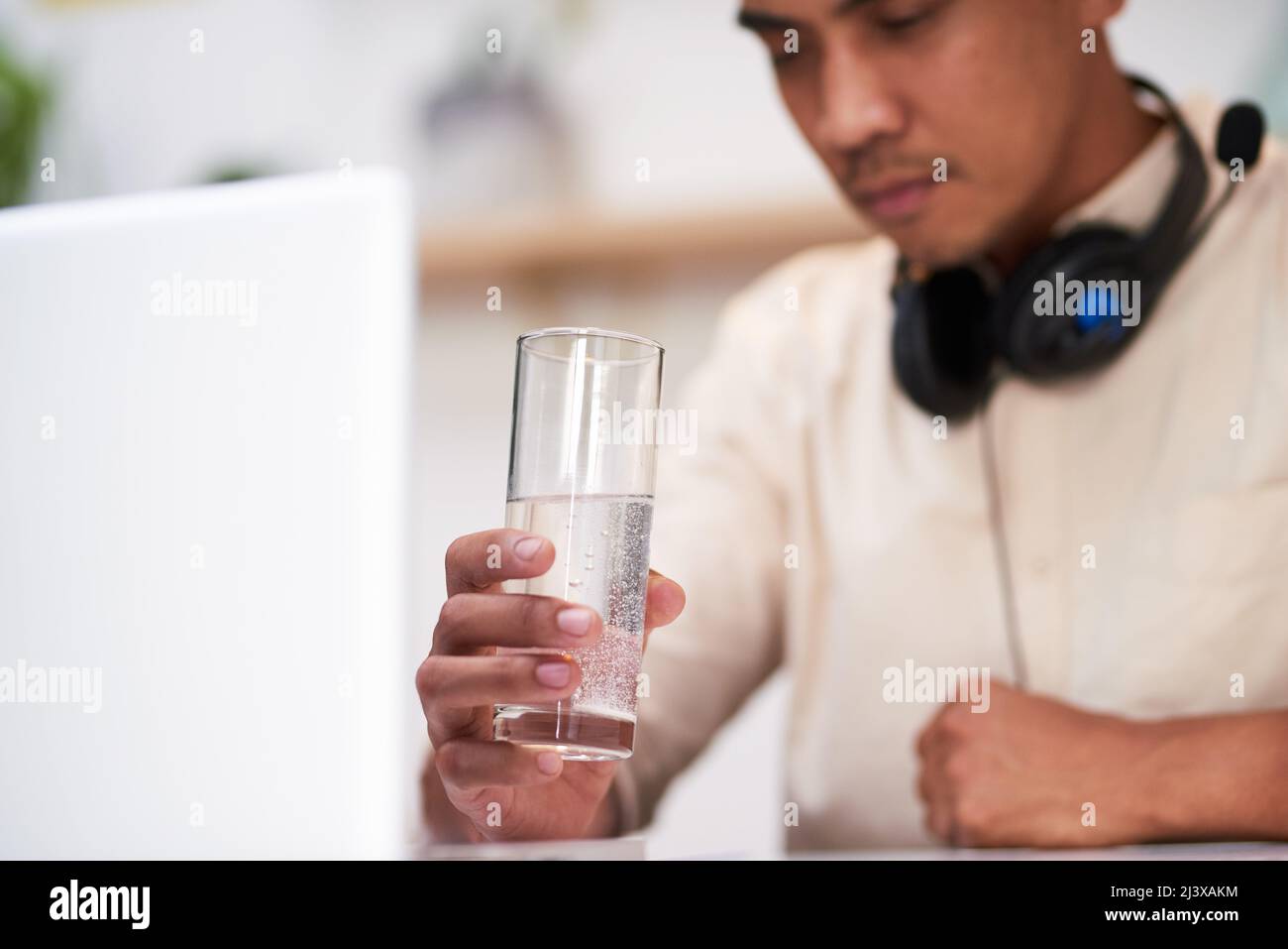 Un uomo asiatico malato aspetta che la sua tavoletta di influenza si sciolga in acqua alla sua scrivania Foto Stock