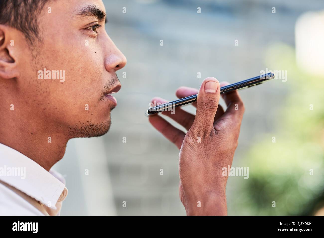 Un primo piano di giovane uomo asiatico invia un voicenote utilizzando il cellulare in città Foto Stock