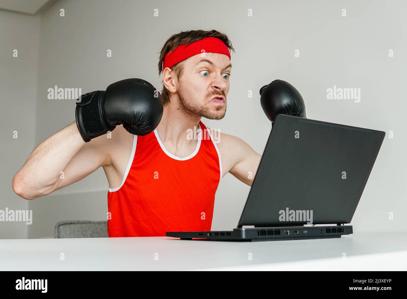 Divertente sportivo arrabbiato che indossa guanti da boxe con un computer portatile. Foto Stock