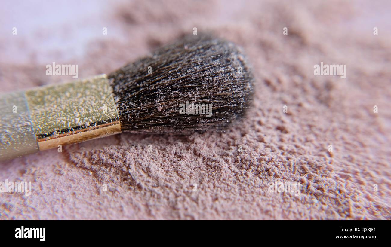 Primo piano di una spazzola make-up, adagiato su una superficie piena di polvere di fondazione cosmetica marrone. Foto Stock