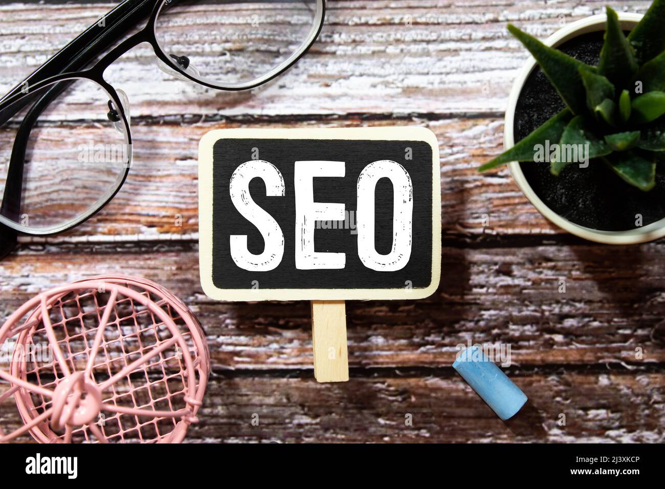 La parola SEO è scritta in un diario quotidiano tra una calcolatrice e una tazza di caffè su un tavolo di legno chiaro. Concetto aziendale Foto Stock