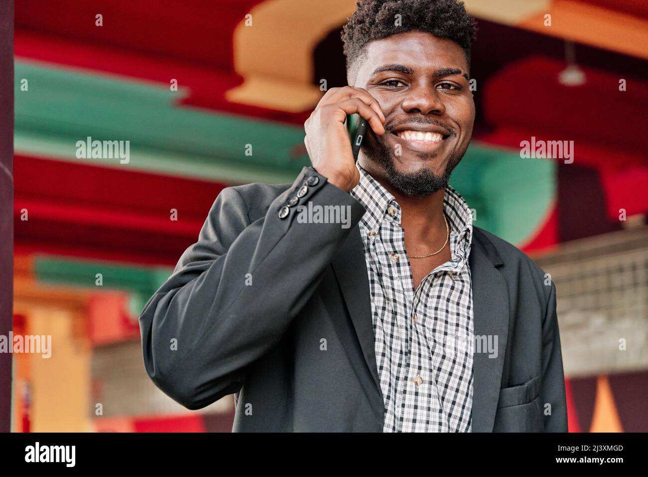 Ritratto di un felice uomo afroamericano che parla su uno smartphone con un colorato sfondo cittadino Foto Stock