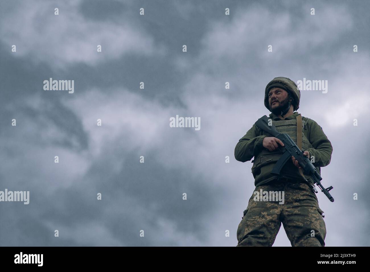 Il soldato ucraino si erge con il fucile d'assalto kalashnikov sullo sfondo del cielo e delle nuvole. Concetto di invasione militare russa in Ucraina. Guerra dentro Foto Stock