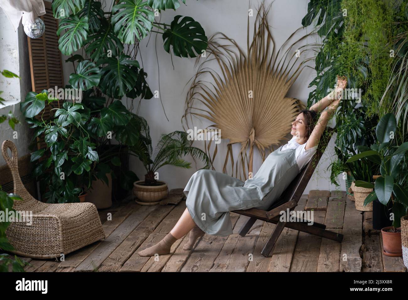 Soddisfatto calmo donna fiorista rilassarsi in giardino interno godere di equilibrio mentale e benessere a casa Foto Stock