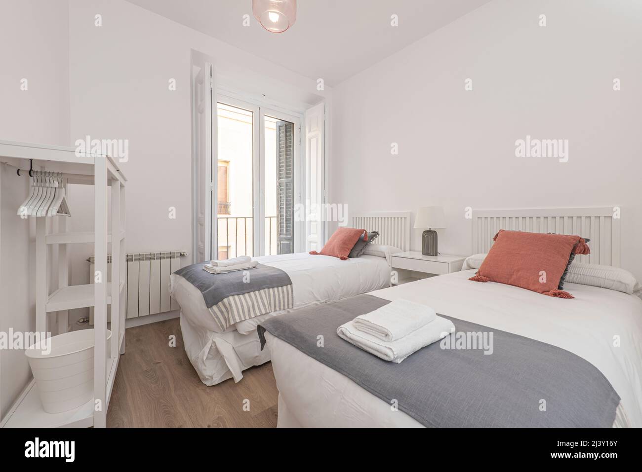 Interno luminoso e moderno della camera da letto con piccolo comodino in  legno, giardino in un barattolo, biancheria da letto bianca, cuscini  colorati e coperta. spazio con pareti blu e parquet in