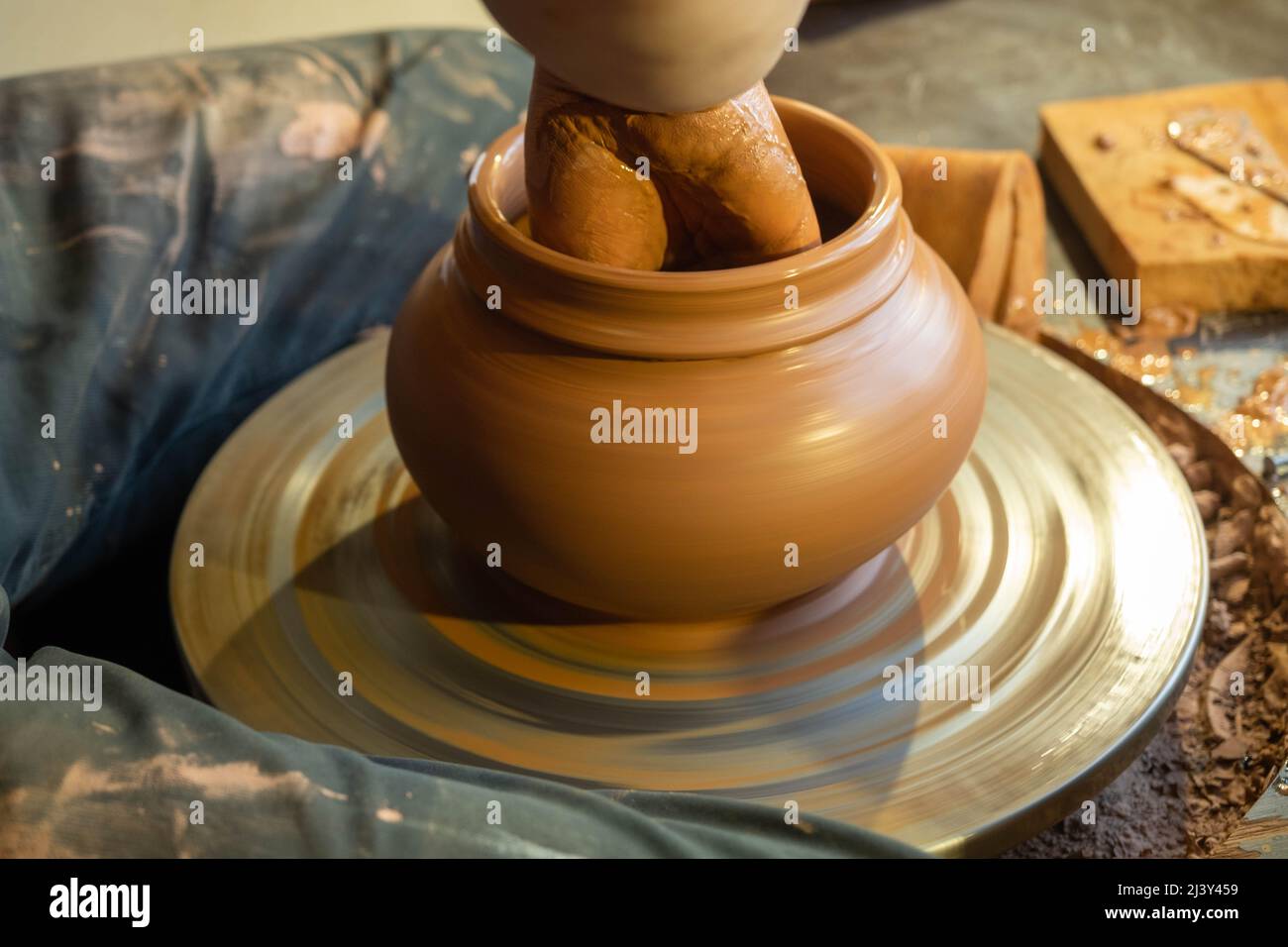 Le mani del vasaio maestro plasmano l'argilla all'esterno. Caraffa di argilla sulla ruota di un vasaio in un laboratorio di ceramica. Foto Stock