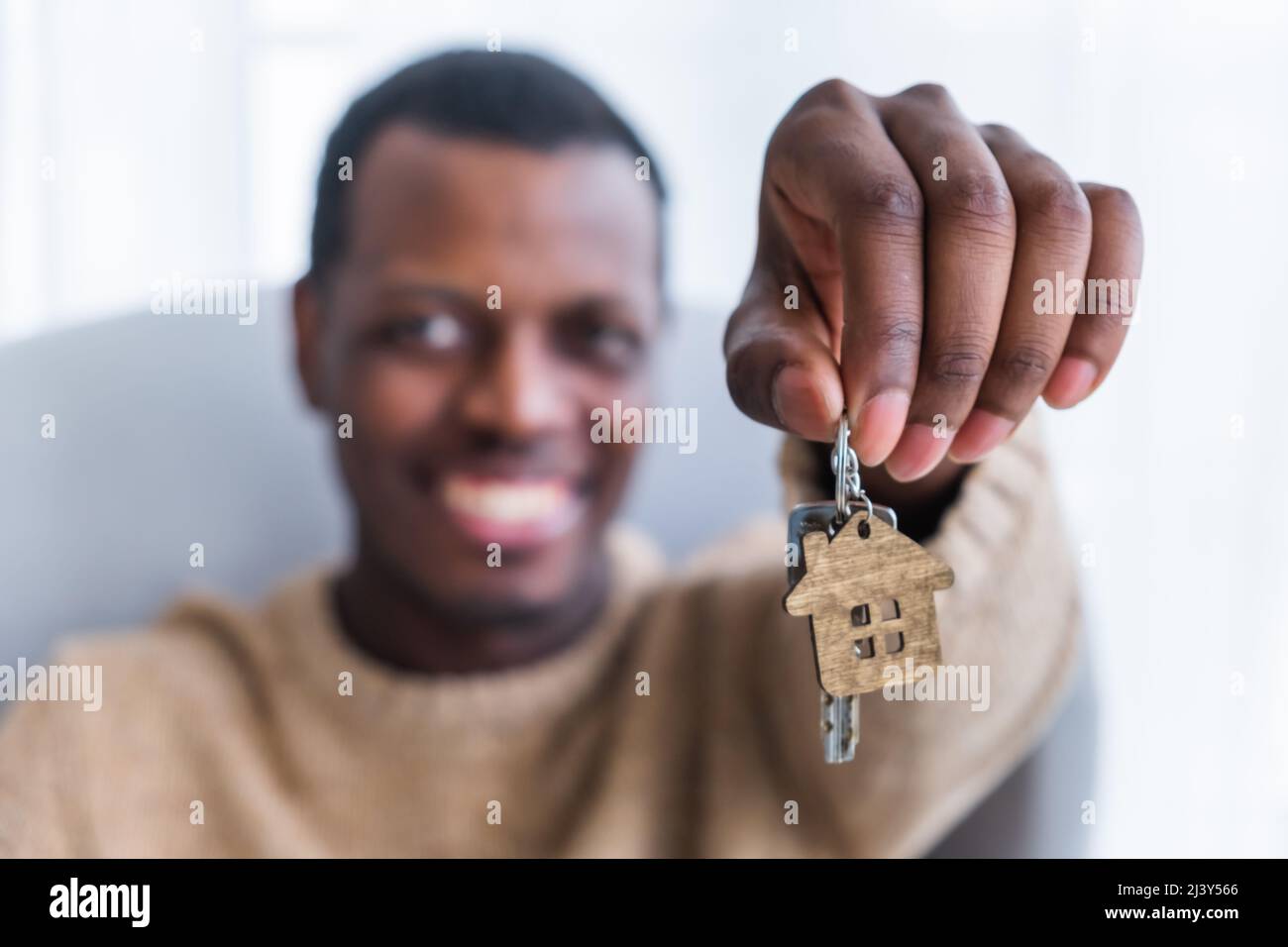 African American uomo brags circa l'acquisto di nuovo appartamento. Focus cambia da chiave con legno casa trinket a felice proprietario di casa vicino vista Foto Stock