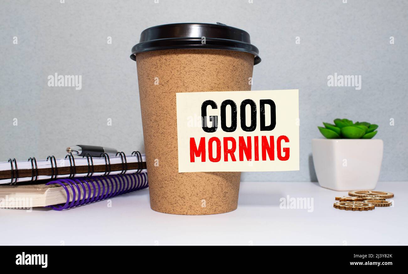 Una tazza di caffè fresco e una nota gialla con questo testo: "Buongiorno". Foto Stock