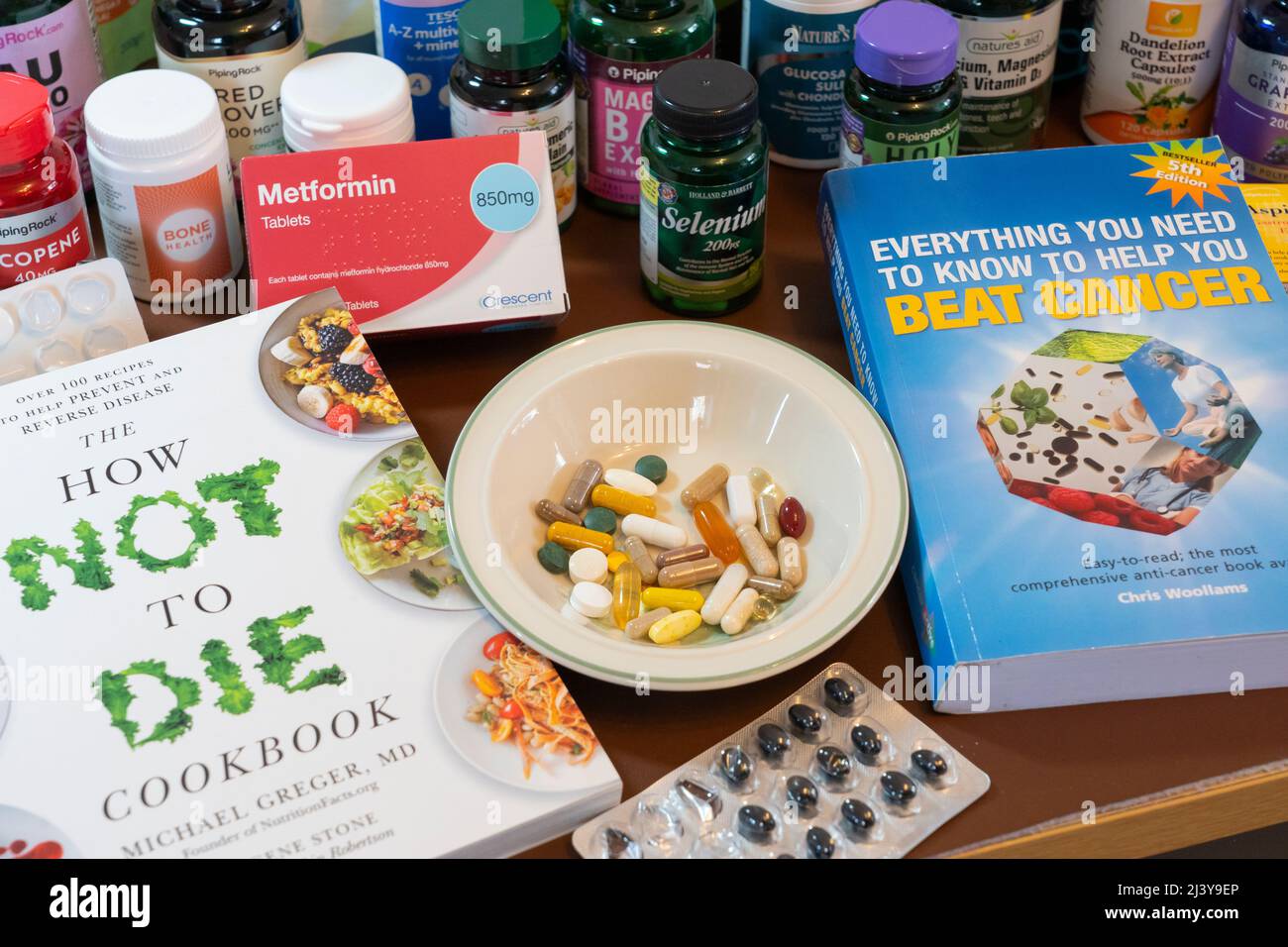 Una selezione dei molti farmaci, vitamine e integratori alimentari presi da qualcuno che cerca di recuperare dal cancro, con libri sul cancro sopravvissuto. REGNO UNITO Foto Stock