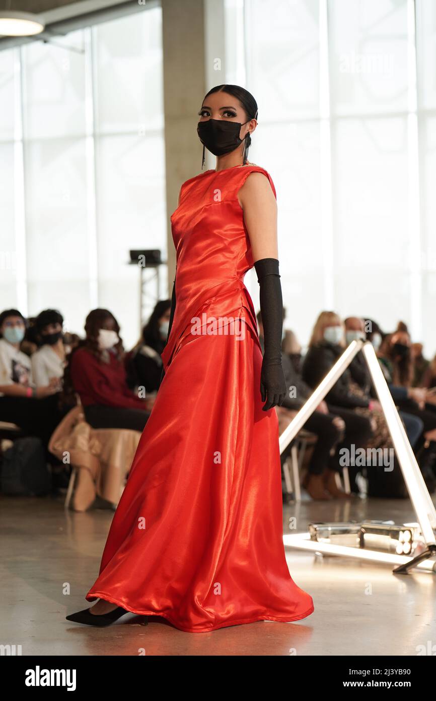 una studentessa asiatica che indossa maschera nera e lungo vestito rosso che cammina lungo la pista di moda Foto Stock