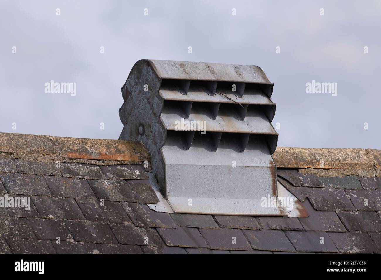 Un metallo galvanizzato, la bocchetta di ventilazione del tetto sulla cresta di un tetto piastrellato di ardesia Foto Stock