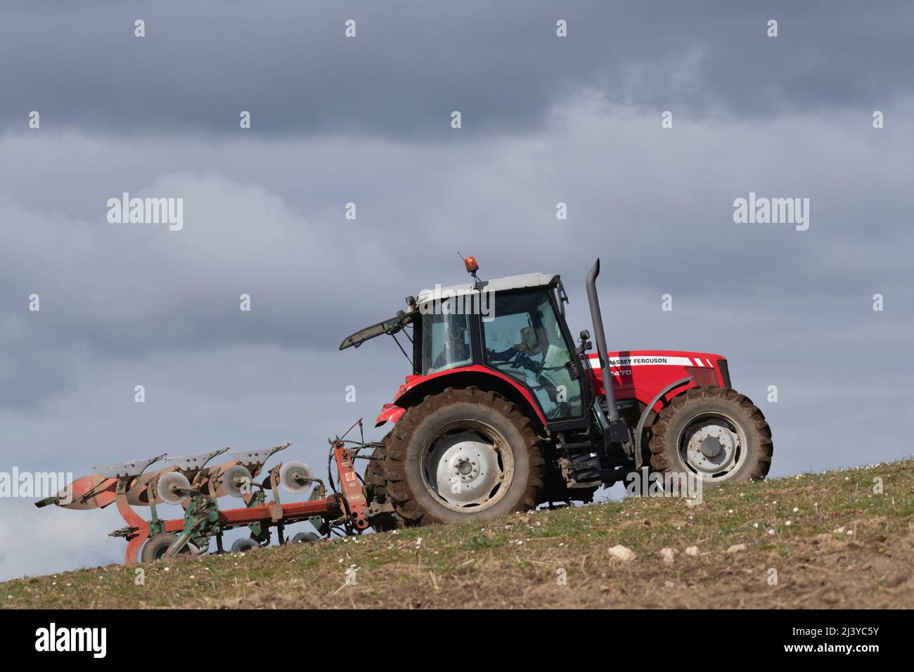 Un trattore rosso Massey Ferguson 5470 che arava Uphill in un campo erboso in una giornata di sole Foto Stock