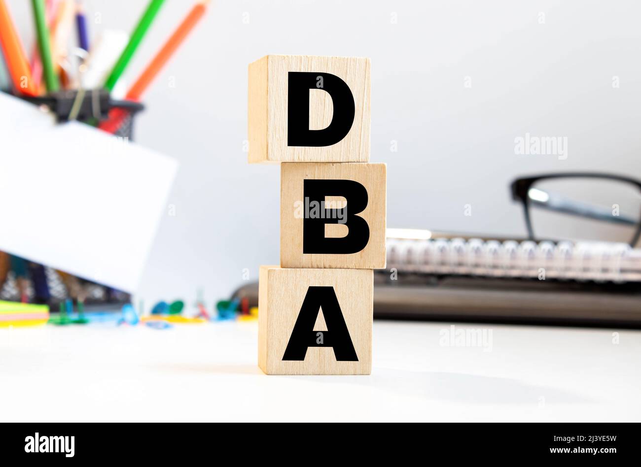 DBA - acronimo da blocchi di legno con lettere, amministratore di database o fare affari come abbreviazione DBA concetto, lettere casuali intorno, grigio backg Foto Stock