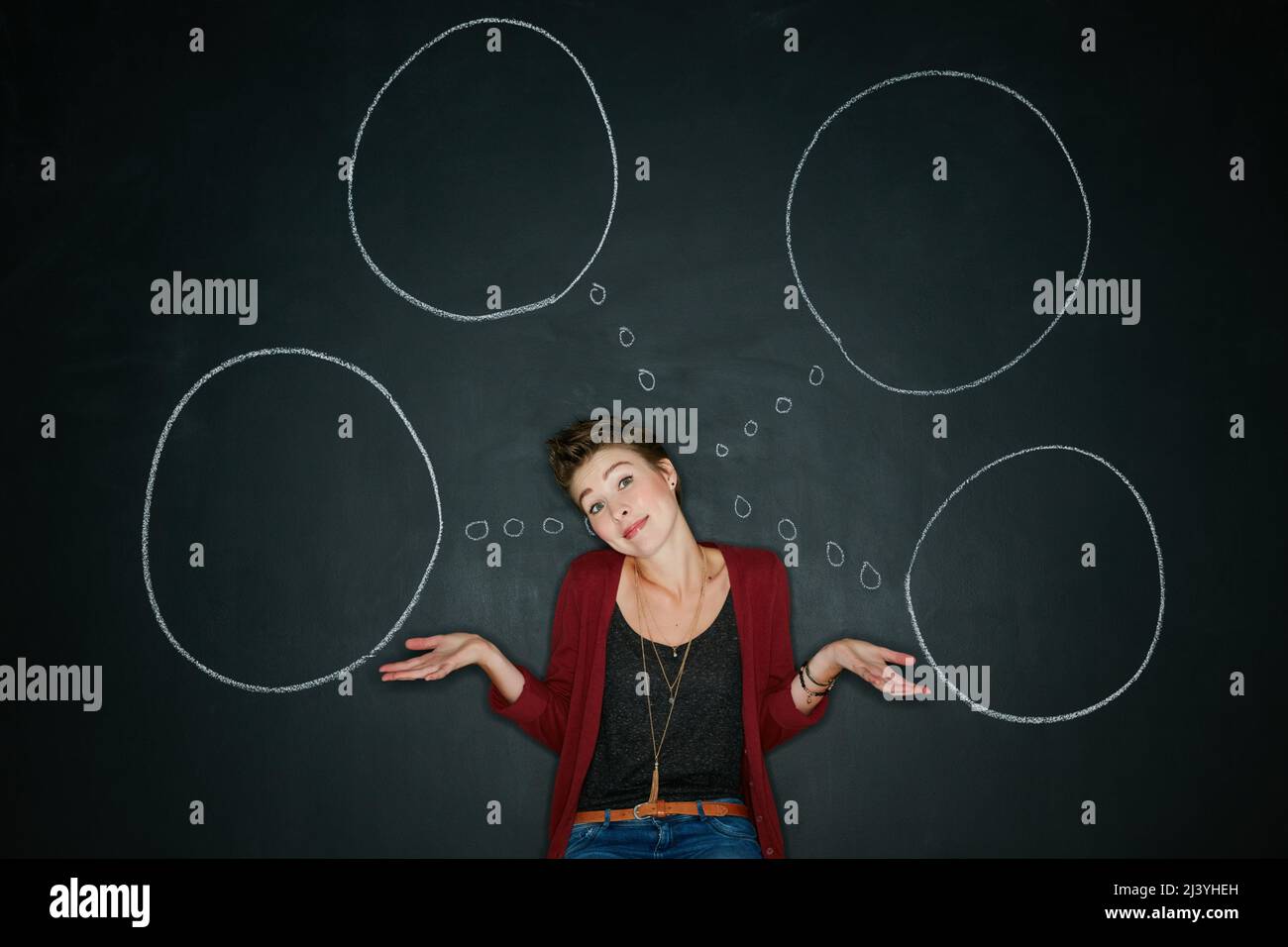 Non ho idea di cosa stia facendo. Studio girato di una giovane donna in posa con un gesso illustrazione di bolle di pensiero su uno sfondo scuro. Foto Stock