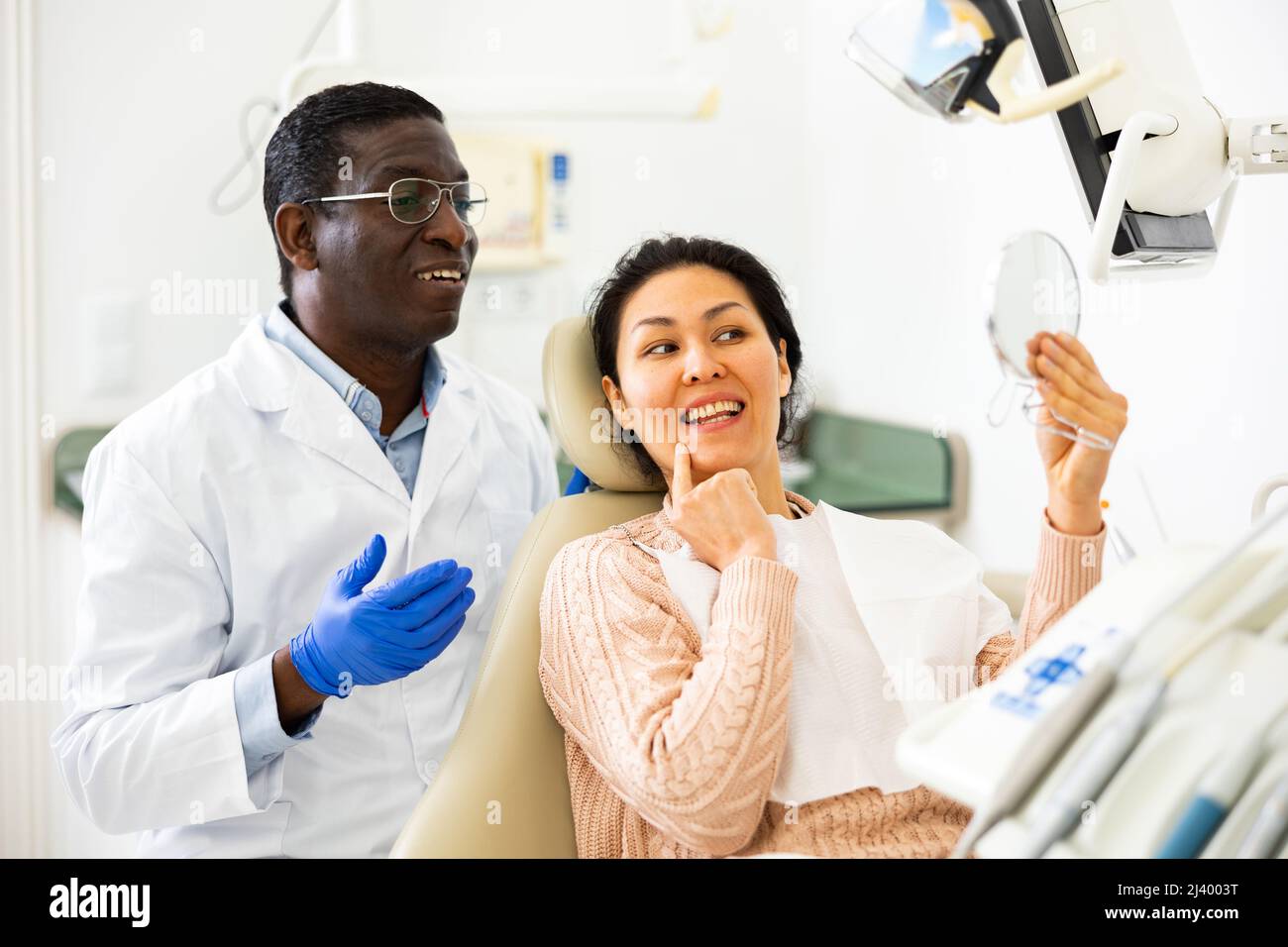 Il paziente dentista guarda nello specchio verso il nuovo dente dopo l'intervento chirurgico Foto Stock