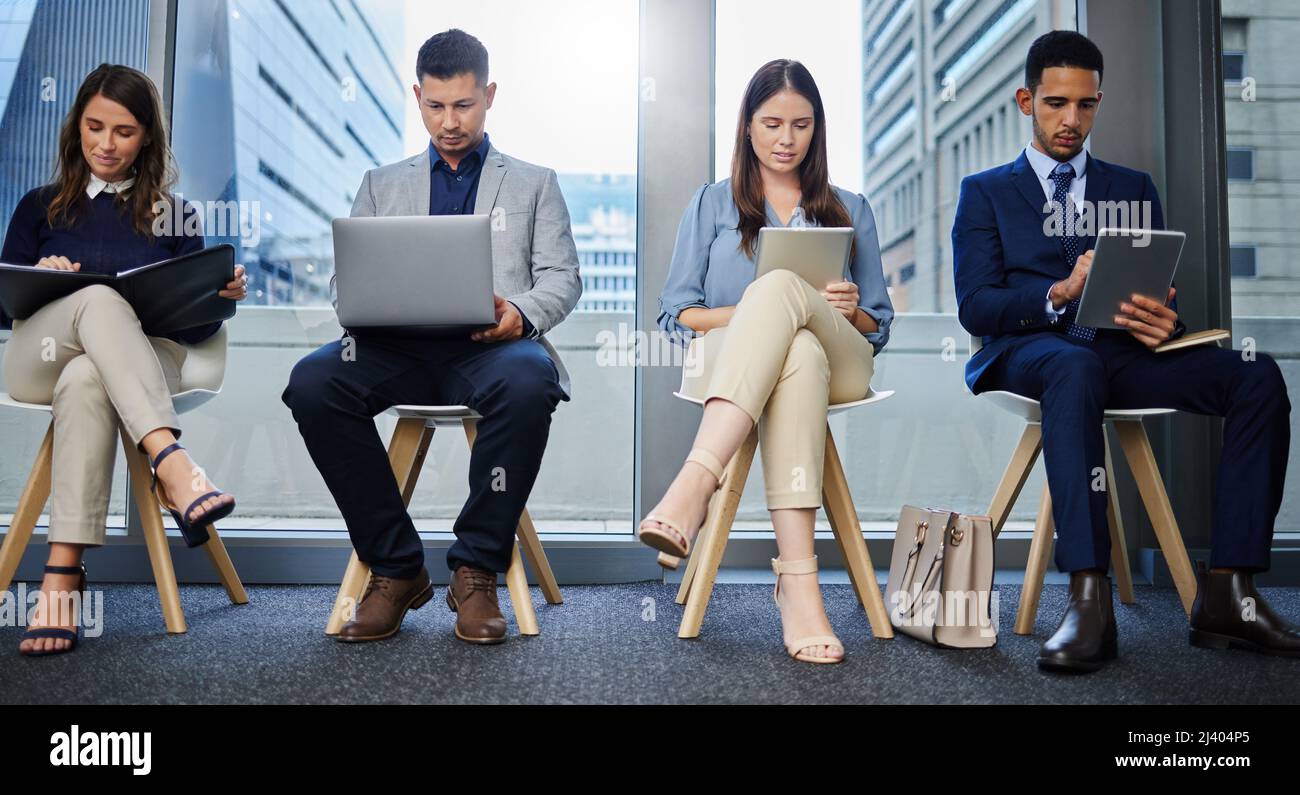 Sempre occupato per tutto il giorno. Scatto di un gruppo di giovani imprenditori che utilizzano dispositivi digitali mentre attendono in linea. Foto Stock