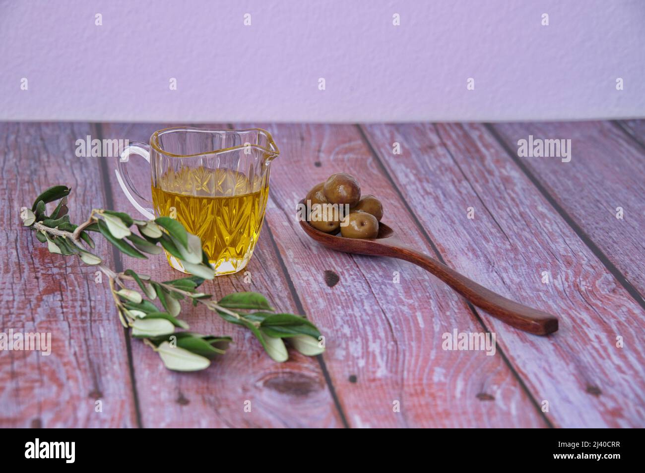 Olive su cucchiaio di legno, olio d'oliva e ramo d'oliva su tavola di legno Foto Stock