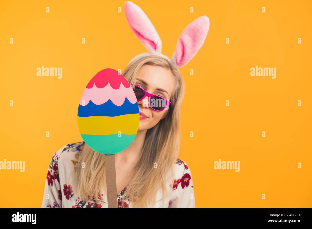 Felice Pasqua - una giovane donna bionda con orecchie conigliere di Pasqua tenendo un grande uovo di Pasqua di legno vacanza concetto arancione sfondo medio primo piano studio shot. Foto di alta qualità Foto Stock