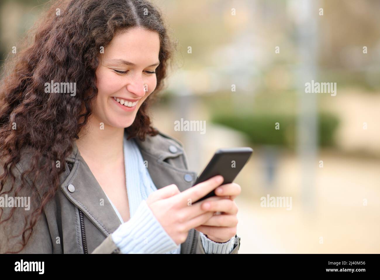 Donna felice che controlla il contenuto del telefono delle cellule che cammina in un parco Foto Stock